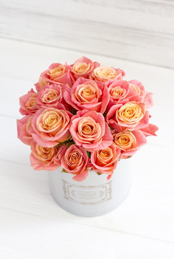 Beautiful pink roses in a round box. Peach roses in a round box. Roses in a round box on a white wooden background.