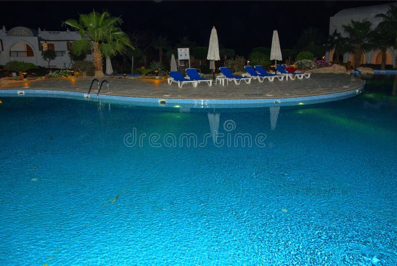 Beautiful pool with clear blue water and reflection of objects in it at night.