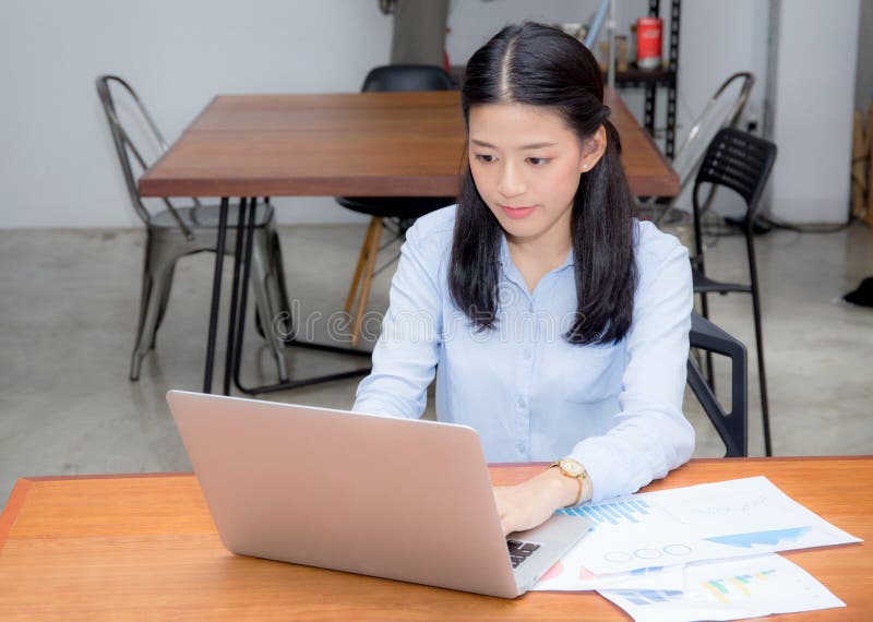 Beautiful of portrait asian young woman working with graph statistic paper on laptop sitting at coffee shop