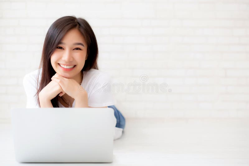 Beautiful of portrait asian young woman working online laptop lying on floor brick cement background, freelance girl using