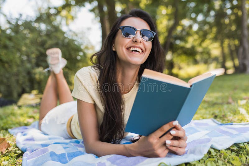 Beautiful portrait of a gorgeous young brunette woman reading a book in the park. Happy female student reading and learning a