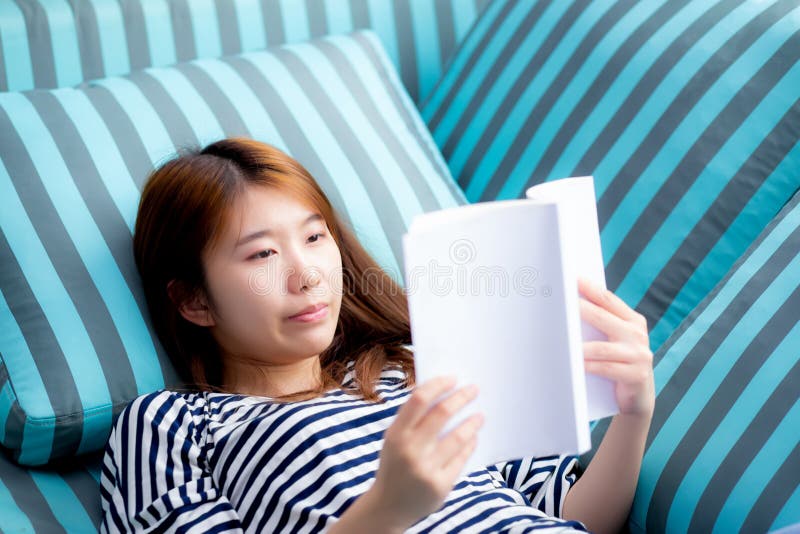 Beautiful of portrait young asian woman relax lying reading book on sofa in bedroom at home