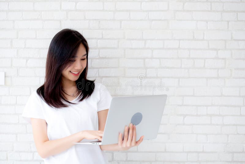 Beautiful of portrait young asian woman smiling and standing holding laptop on brick cement wall background stock image Beautiful of portrait young asian woman smiling and standing holding laptop on brick cement wall background stock image