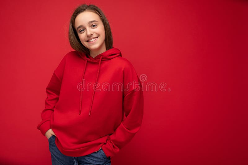 Beautiful positive smiling brunet little lady wearing stylish red hoodie standing isolated over red background wall