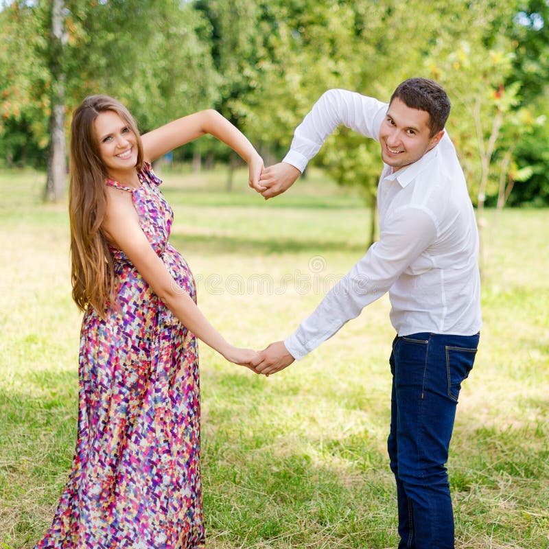 Beautiful pregnant couple happy together expecting a child. Man and woman walking in the park showing heart with hands. Share the. Autumn, longhair.