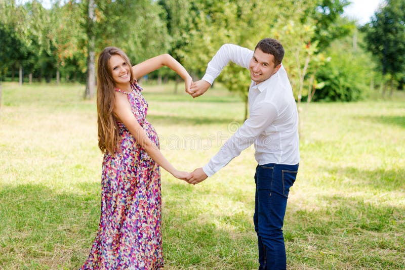 Beautiful pregnant couple happy together expecting a child. Man and woman walking in the park showing heart with hands. Share the. Human, heterosexual.