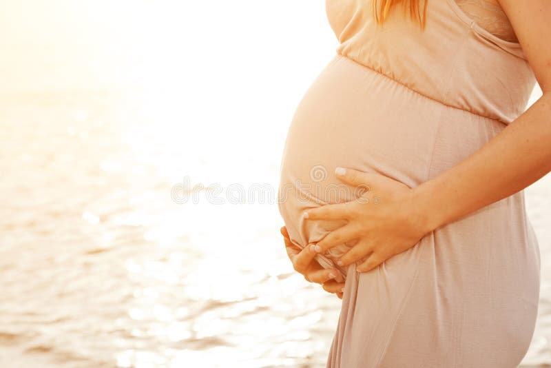 A beautiful pregnant woman on the beach touching her belly