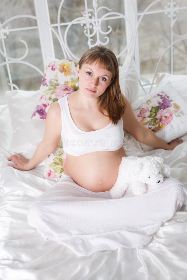 Beautiful pregnant woman posing while siting on a bed