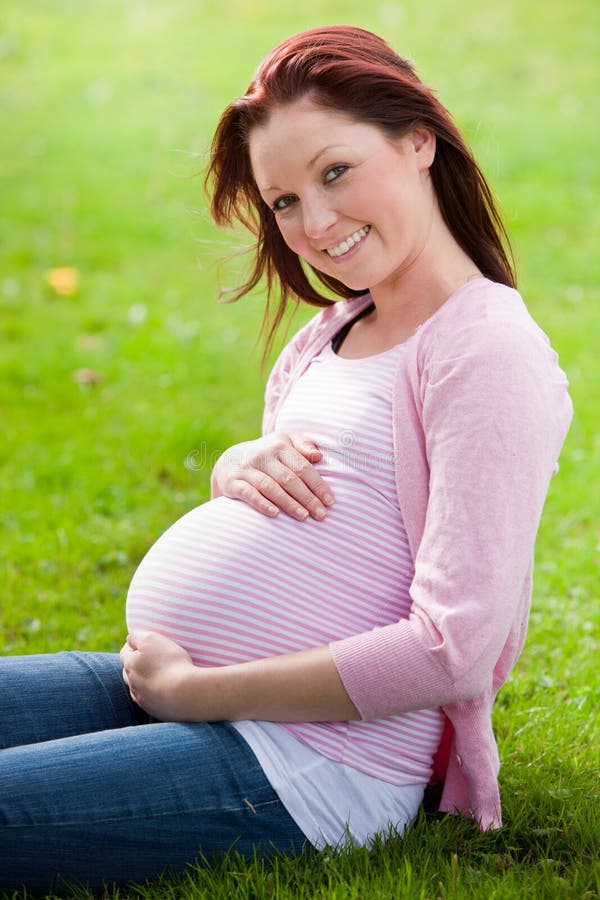 Beautiful pregnant woman sitting on the grass