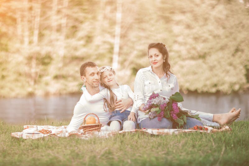 Pregnant woman with a bouquet of lilacs and her family sitting on the grass near the river royalty free stock photography Pregnant woman with a bouquet of lilacs and her family sitting on the grass near the river royalty free stock photography