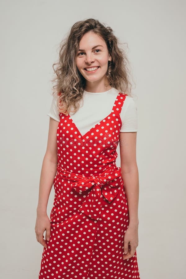 A beautiful primary school teacher. A girl in a bright red summer dress. A curly girl with a dazzling smile. Red dress in white polka dots. High quality photo