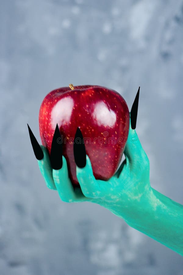 Beautiful red apple in green hands of old witch with black nails.