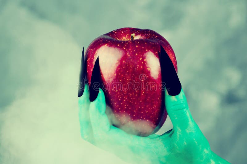 Beautiful red apple in green hands of old witch with black nails.