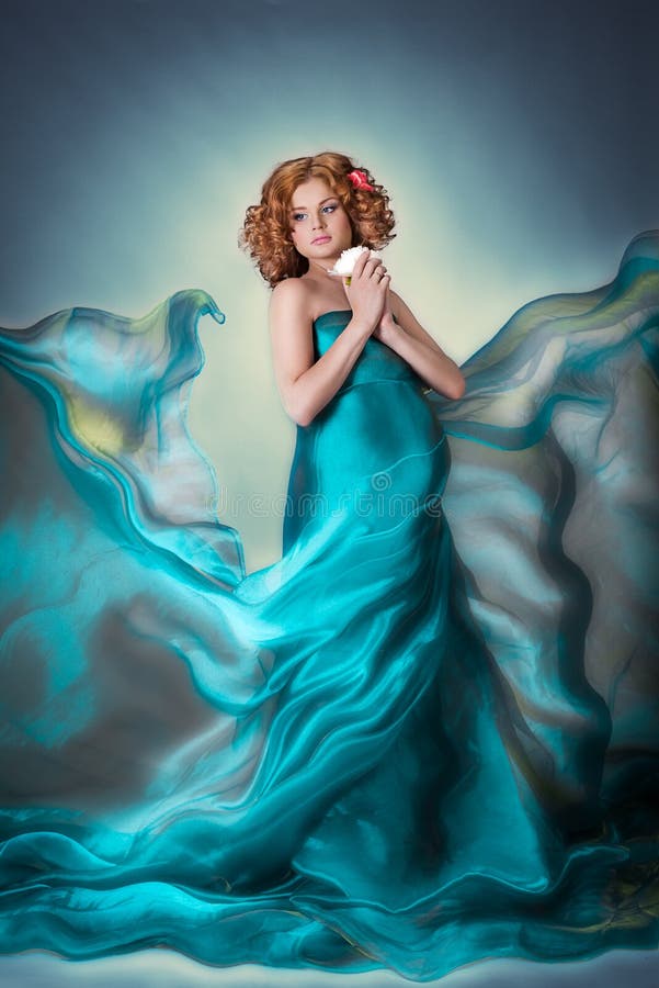 Beautiful red hair Pregnant tender woman in blue flying organza fabric dress with flower