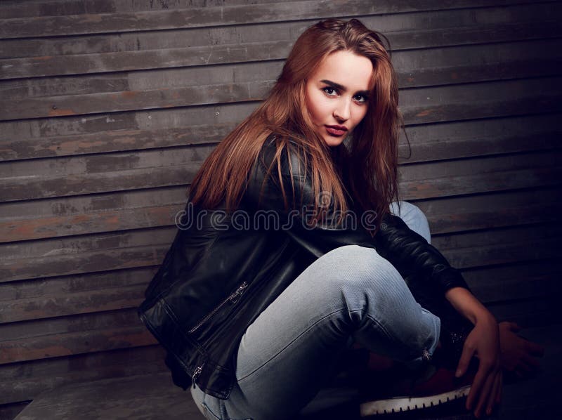 Beautiful red hair woman sitting on the stone in black jacket an