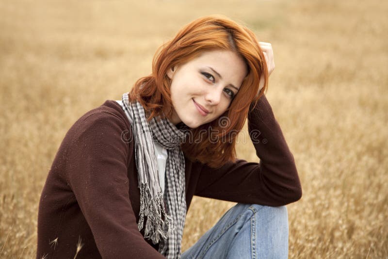 Beautiful red-haired girl at yellow autumn grass.