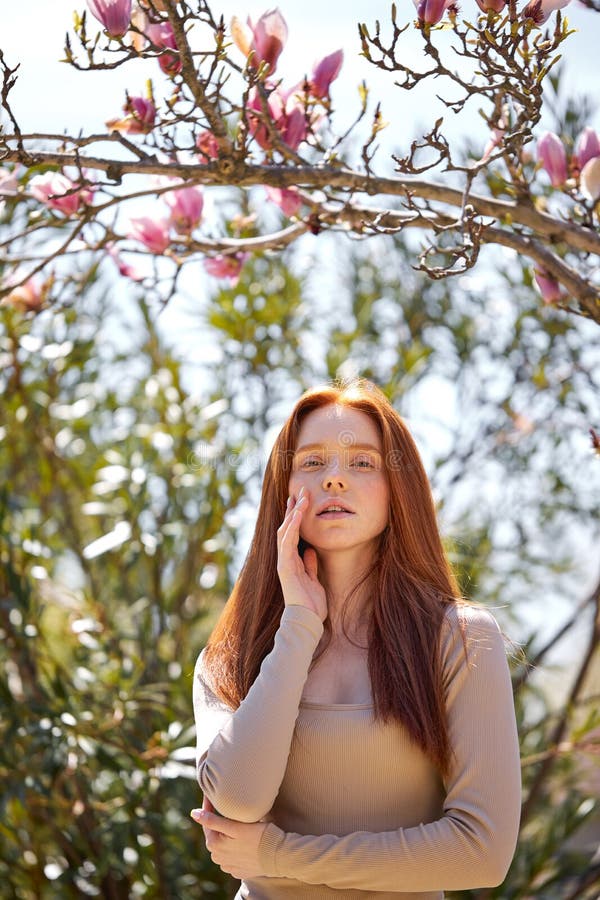 Beautiful Redhead Woman In Blossoming Garden Touching Face Sensually Posing At Camera Stock