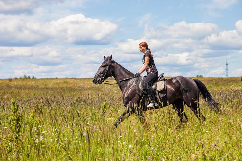 Beautiful redheaded girl riding a horse in countryside. Teen girl rides on the field with grass on a Sunny summer day royalty free stock photos Beautiful redheaded girl riding a horse in countryside. Teen girl rides on the field with grass on a Sunny summer day royalty free stock photos