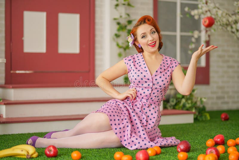 Beautiful redheaded pin up girl in pink polka dot dress and vintage stockings posing near the entrance of her home