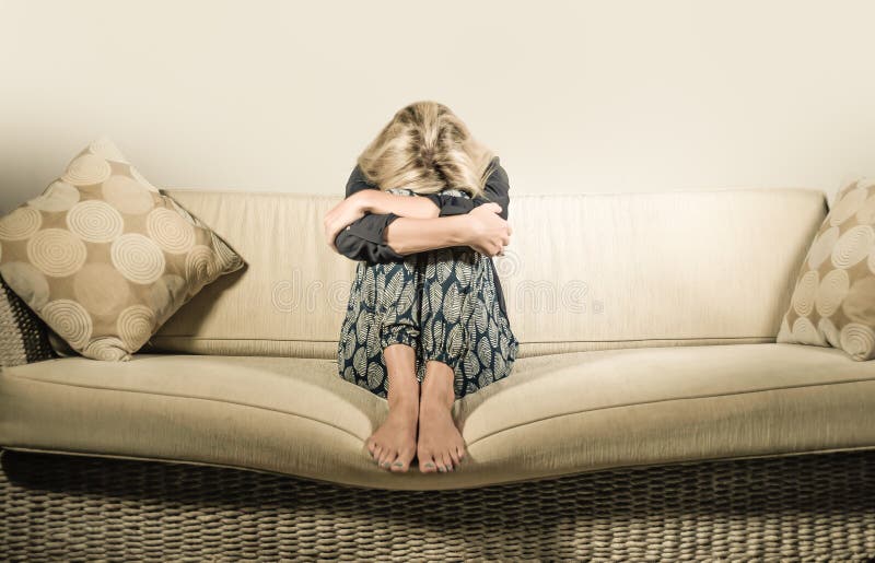 Beautiful 40s woman depressed at home - dramatic portrait of sad and desperate blonde girl on couch suffering depression problem