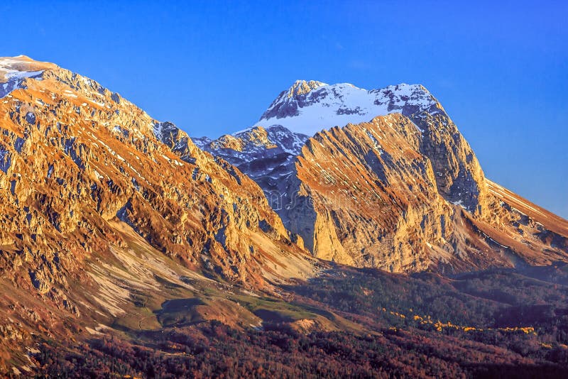 Beautiful scenic golden autumn landscape of Fisht mountain peak at sunset under blue sky, West Caucasus, Russia