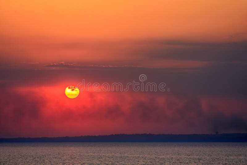 Scenic landscape of sun setting by lake with clouds over horizon.