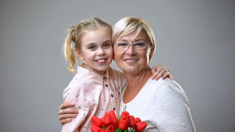 Beautiful senior lady holding flowers gift from granddaughter and hugging, love stock image Beautiful senior lady holding flowers gift from granddaughter and hugging, love stock image