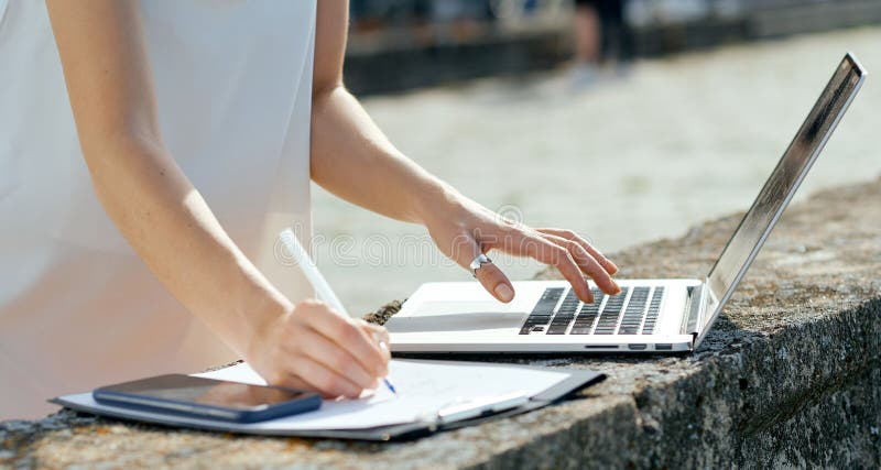 Beautiful, serious girl in a white dress with a tablet, pen, laptop phone on the dock