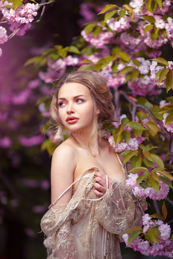 Beautiful adult girl standing at blossoming tree in the garden