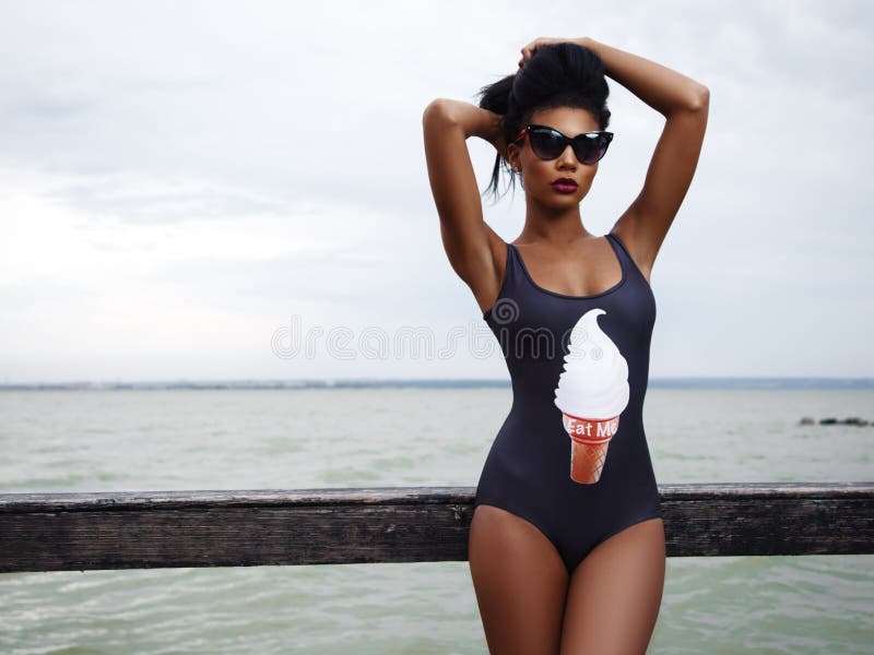 Beautiful, and attractive woman with slim tanned body in trendy swimwear and sunglasses is posing near the rail on seafront stock images Beautiful, and attractive woman with slim tanned body in trendy swimwear and sunglasses is posing near the rail on seafront stock images