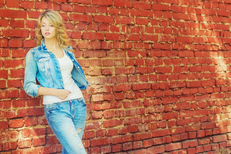 Beautiful blonde woman standing near a brick wall in a denim jacket and pants