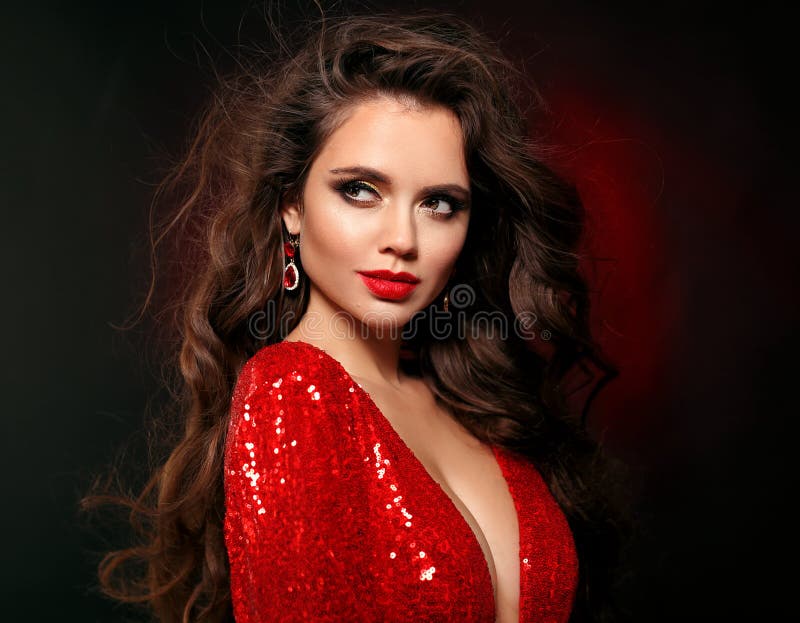 Beautiful sexy brunette in red dress with healthy curly hair and glamour makeup. Fashion Beauty Girl  on black studio Background