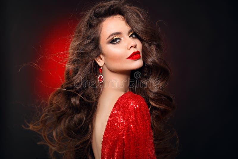 Beautiful sexy brunette in red dress with healthy curly hair and glamour makeup. Fashion Beauty Girl Isolated on black studio