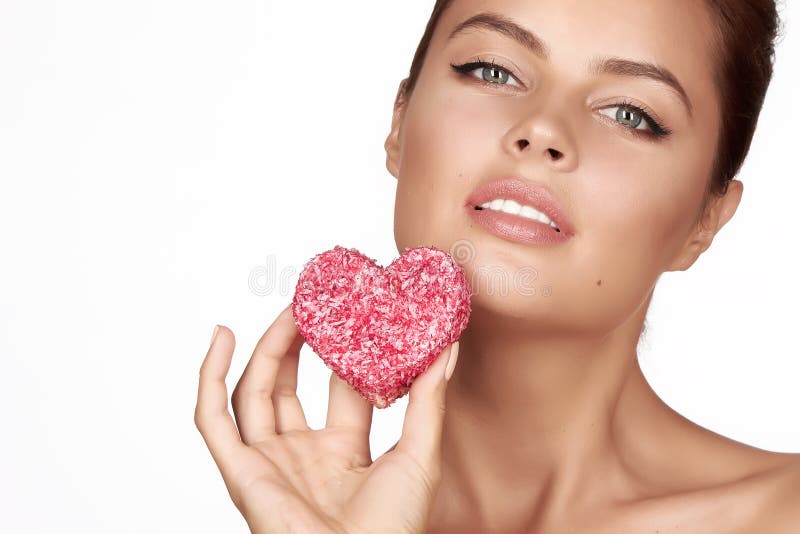 Beautiful brunette woman eating cake shape of heart on a white background, healthy food, tasty, organic, romantic valentine d