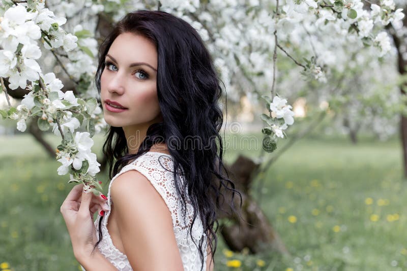 Beautiful girl with long dark hair in a white summer sundress walking in the garden in a blossoming apple trees photo in gent stock photography Beautiful girl with long dark hair in a white summer sundress walking in the garden in a blossoming apple trees photo in gent stock photography