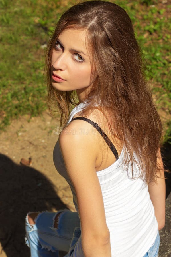 Beautiful girl with long hair in a white t-shirt and jeans sitting in the woods on a Sunny day