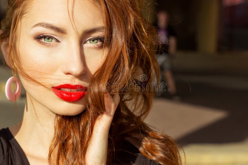 Beautiful girl with red hair with big red lips with makeup in the city on a Sunny summer day