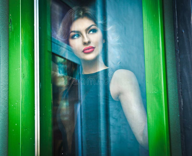Beautiful woman posing in a green painted window frame, shot through window. gorgeous young female with long curly hair royalty free stock photo Beautiful woman posing in a green painted window frame, shot through window. gorgeous young female with long curly hair royalty free stock photo