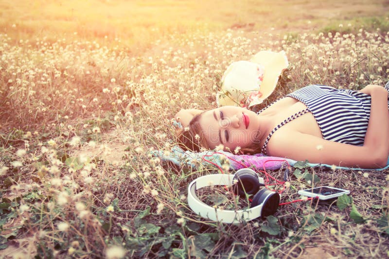 Beautiful young woman lying nearing headphone in the flower