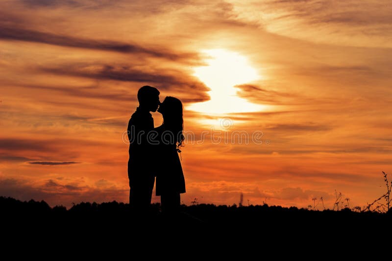 Beautiful shade loving happy couple kissing at sunset in a field of warm summer day