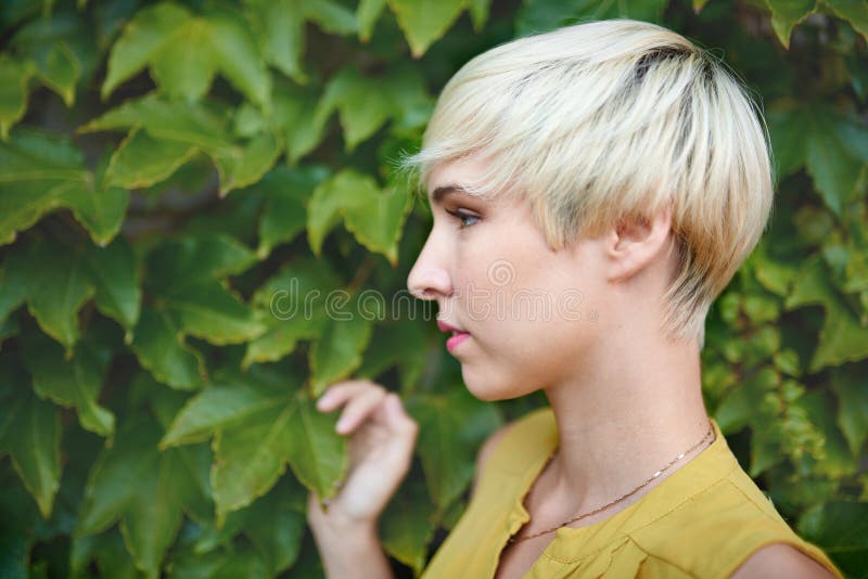 Beautiful short haired platinum blond woman standing against an ivy fence backdrop