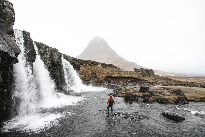 Beautiful shot of a person standing in the water near waterfalls flowing down the hills.