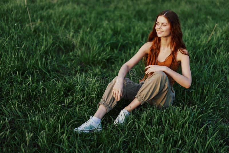 A Beautiful Skinny Woman Sits on the Grass in Casual Clothes and ...