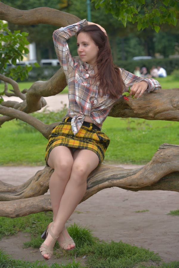 Slender Brunette Girl In A Plaid Skirt And Blouse In The Summer By A