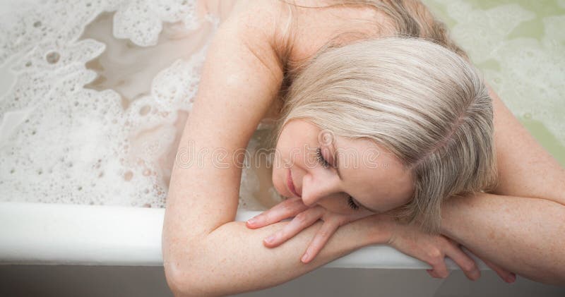 A beautiful smiling girl with blond hair sits in a bath and washes, in the bathroom. An image about cleanliness and about taking care of yourself and your body