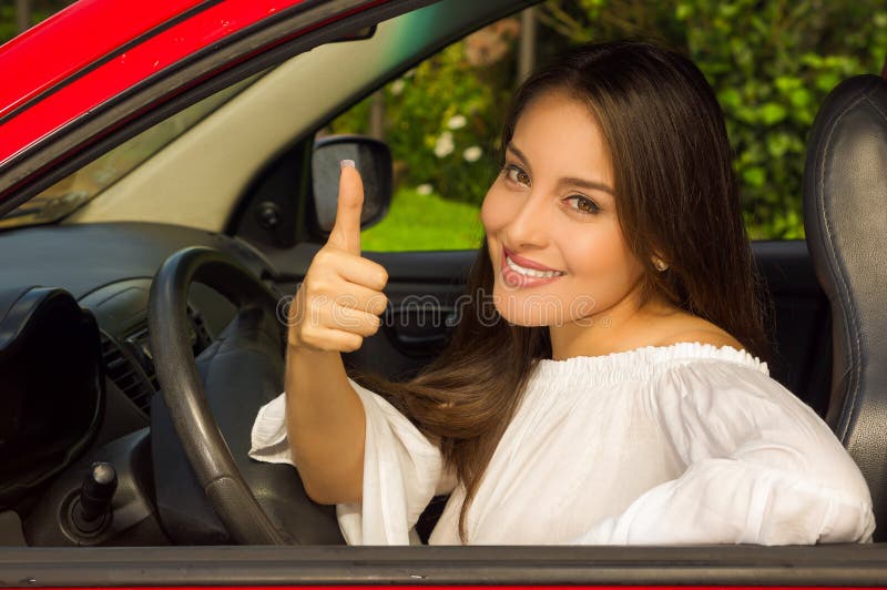 Beautiful smiling girl in red car with thumbs up signal of victory