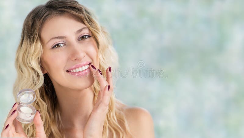 Beautiful smiling girl with wavy hair using lip balm or gloss.  Young blonde woman applying make-up cosmetic SPA product