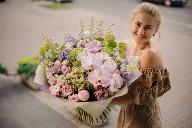 Beautiful smiling woman holds large bouquet with orchids and other flowers