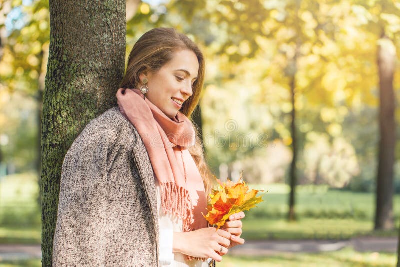 Beautiful smiling woman dreams and holding autumn yellow maple leaf outdoors. Romantic girl in fall park. royalty free stock photos Beautiful smiling woman dreams and holding autumn yellow maple leaf outdoors. Romantic girl in fall park. royalty free stock photos