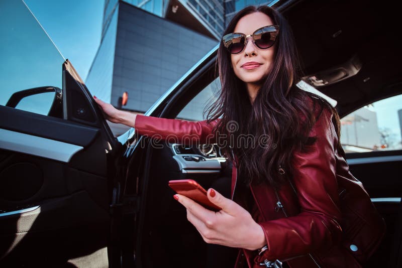 Beautiful smiling women is posing in her new car while chatting on mobile phone